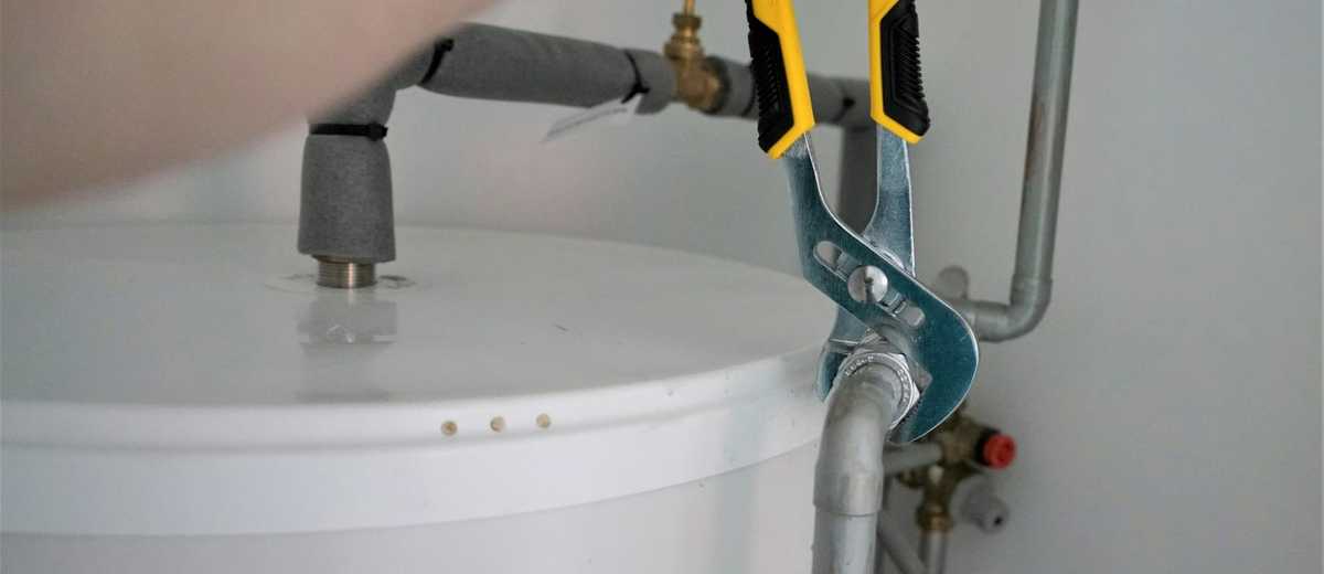 A plumber tightening a valve on a water heater with a wrench