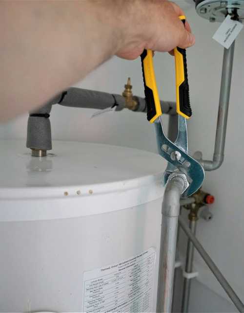 A plumber tightening a valve on a water heater with a wrench