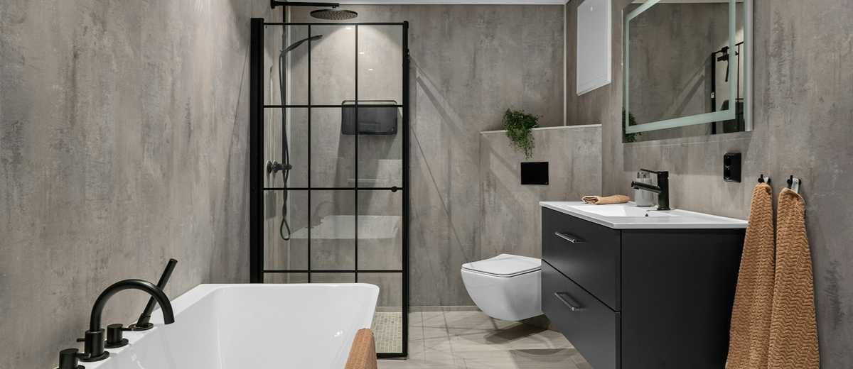 A finished bathroom with a bath, a wall-hung toilet and a black shower screen
