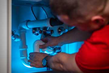 A plumber working on the drain pipes inside a sink cabinet