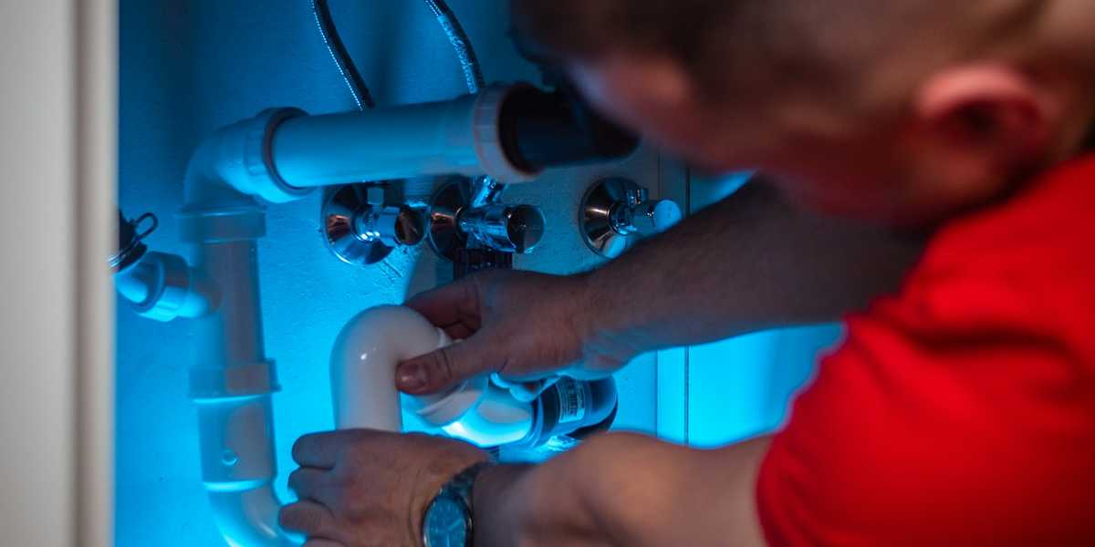 A plumber working on the drain pipes inside a sink cabinet