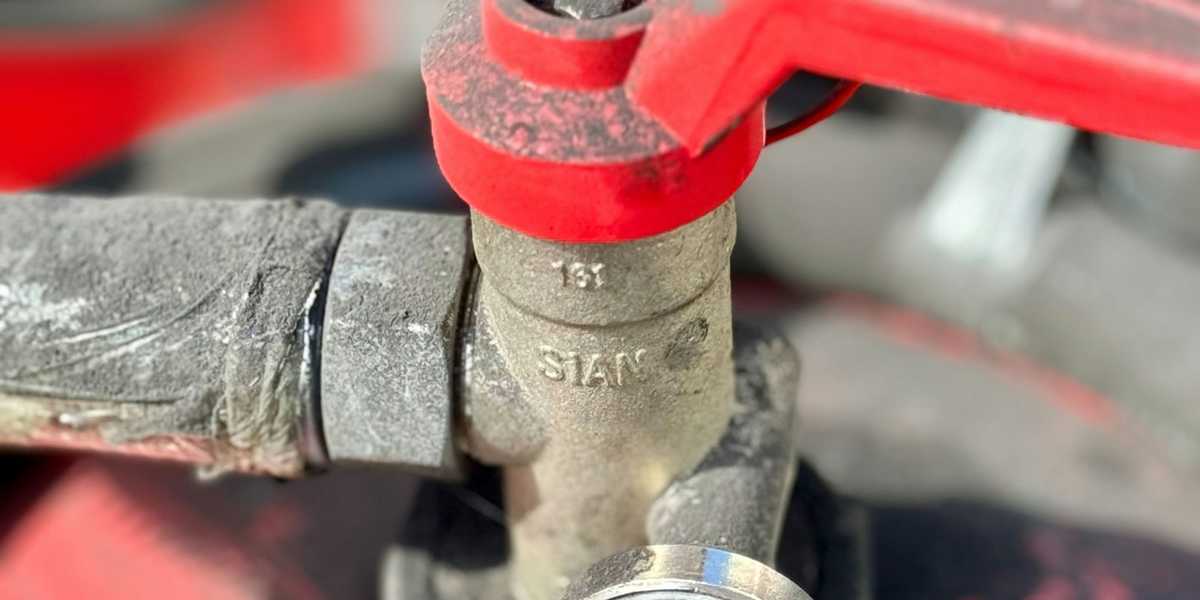 A red valve wrench on a pipe next to a pressure gauge