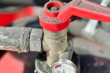 A red valve wrench on a pipe next to a pressure gauge