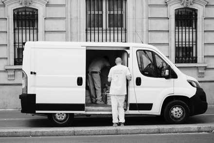 Two workers loading a white van parked on a city street